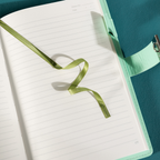 Close-up of the open lined paper interior with a green satin ribbon bookmark and a patterned pen.