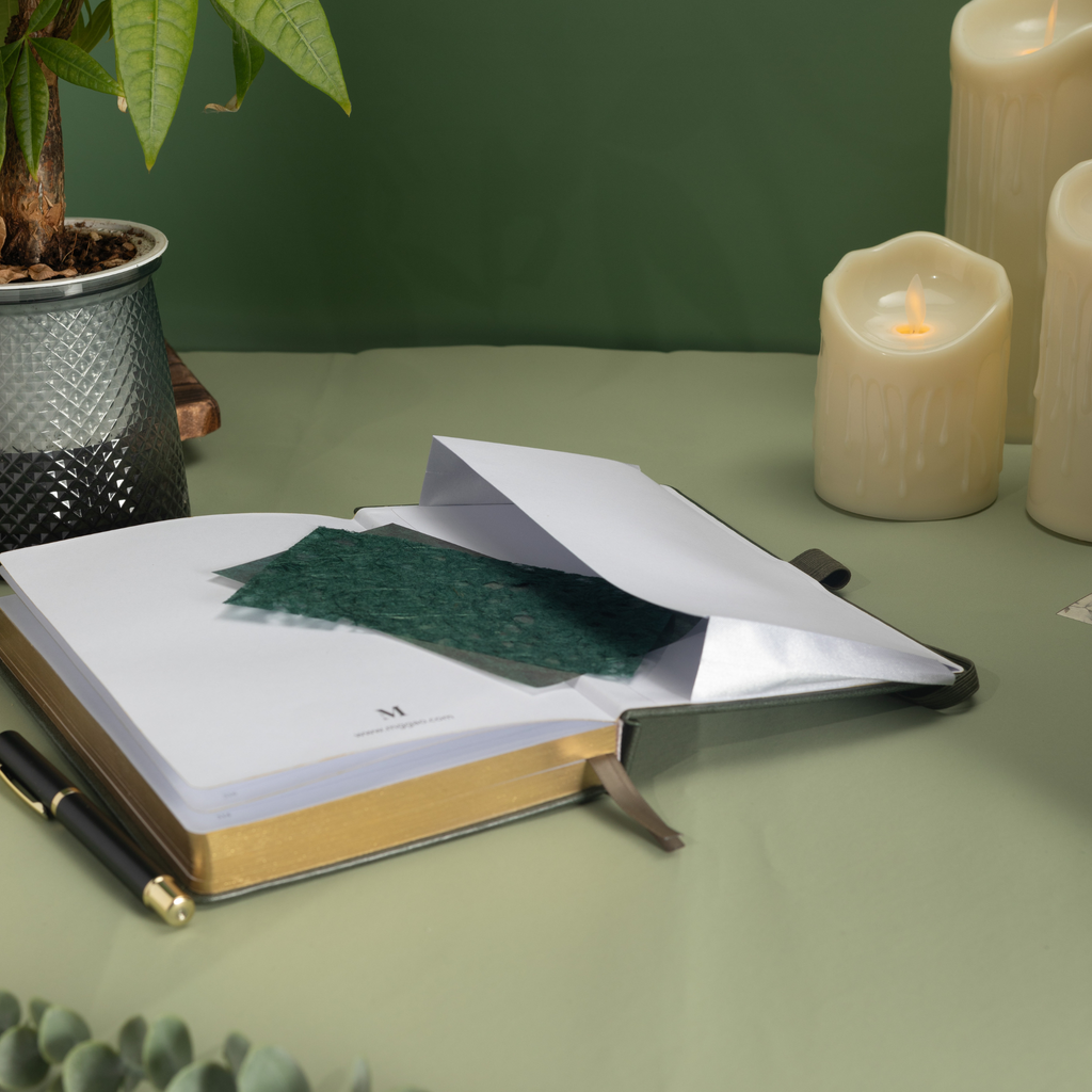Inner back pocket of the dark green vegan leather notebook holding a green card, with gold gilded edges visible and styled next to a feather pen.  