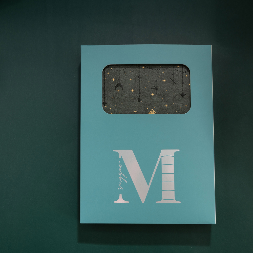 Light blue window-cut gift box featuring a white "M" logo, displaying the dark green mountain vegan leather notebook inside.