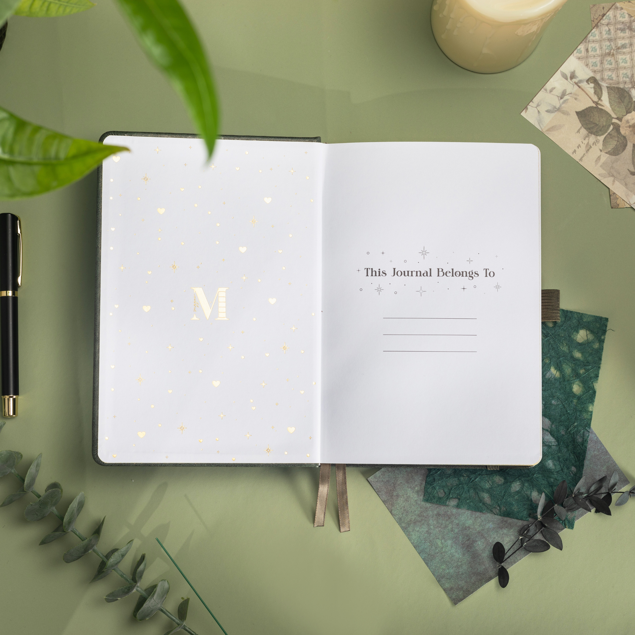 Inside opening page of the dark green mountain journal featuring a gold foil "M" logo and "This Journal Belongs To" ownership section.