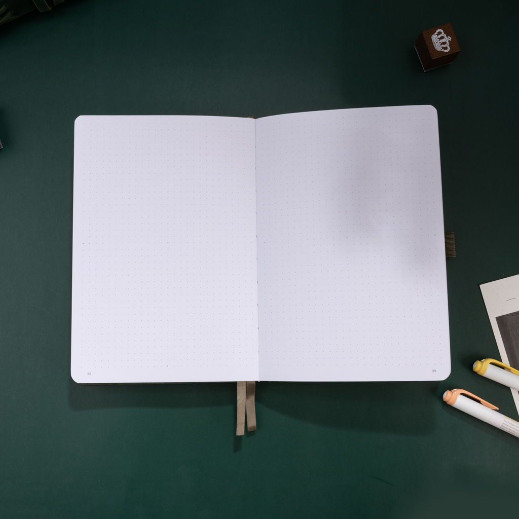 Open A5 journal laid flat, displaying the clean 160gsm dot grid paper interior and a green ribbon bookmark. 