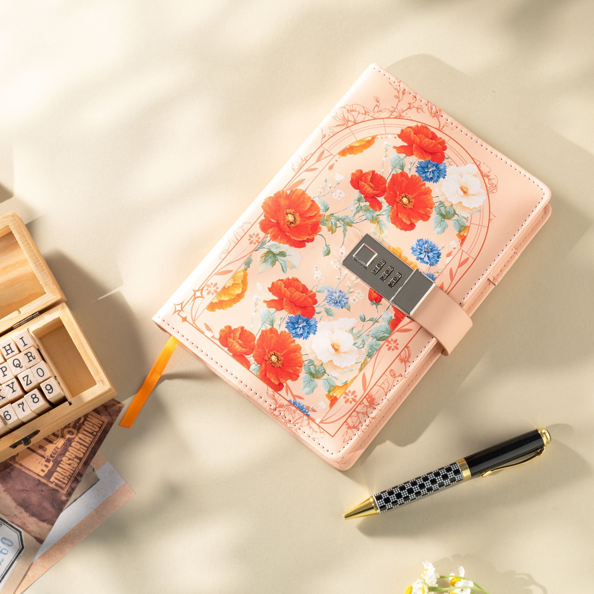 Top-down view of the orange vegan leather notebook laid flat, featuring a vibrant floral arch design, a 3-digit metal combination lock, and an orange ribbon bookmark, styled with wooden alphabet stamps and a patterned pen.