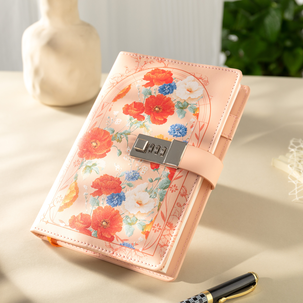 Angled view of the orange vegan leather notebook with a metal combination lock, showcasing the colorful floral arch design, smooth cover texture, and matching orange elastic strap, styled with a pen on a light desk.