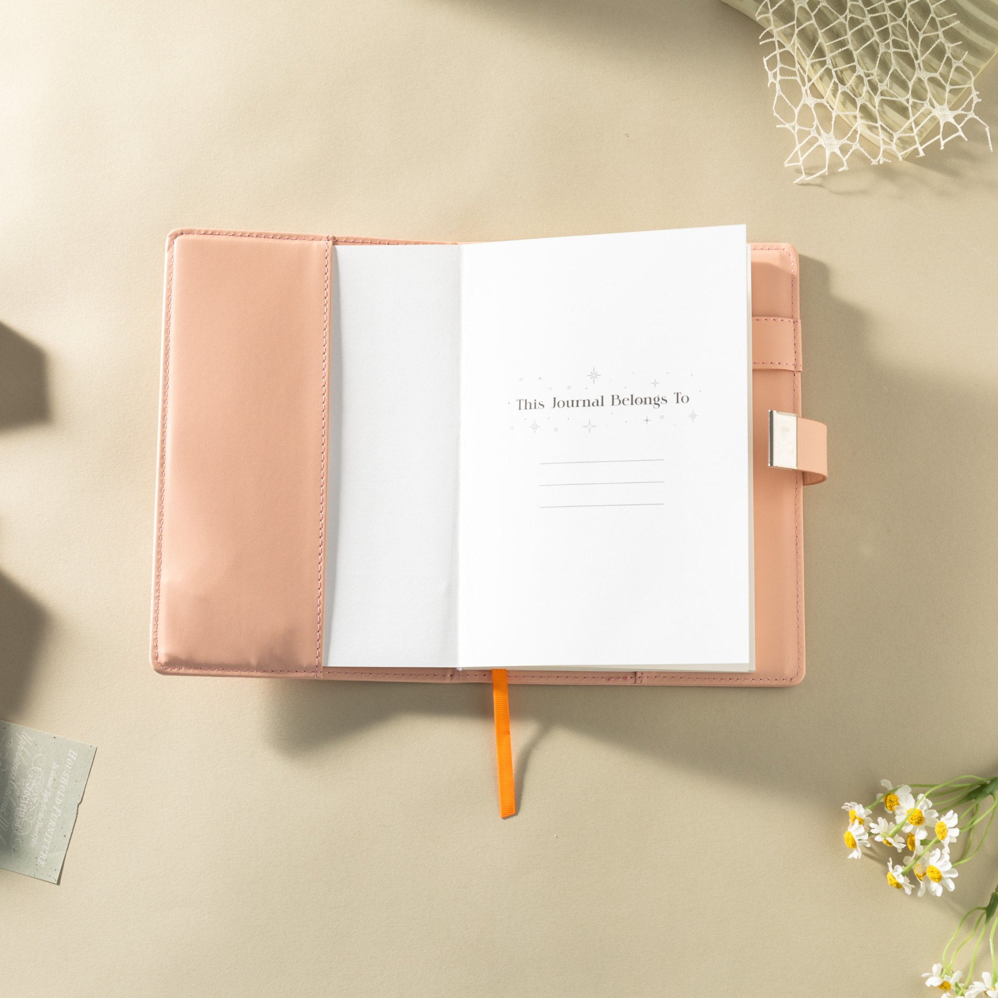 Open orange vegan leather notebook showing the "This Journal Belongs To" ownership page, laid flat with a matching orange ribbon.