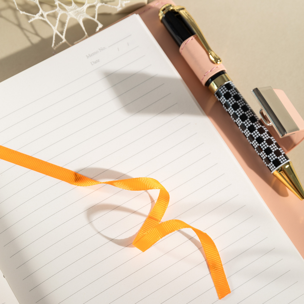Close-up of the open lined paper interior with a bright orange satin ribbon bookmark and a patterned pen.