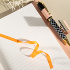 Close-up of the open lined paper interior with a bright orange satin ribbon bookmark and a patterned pen.