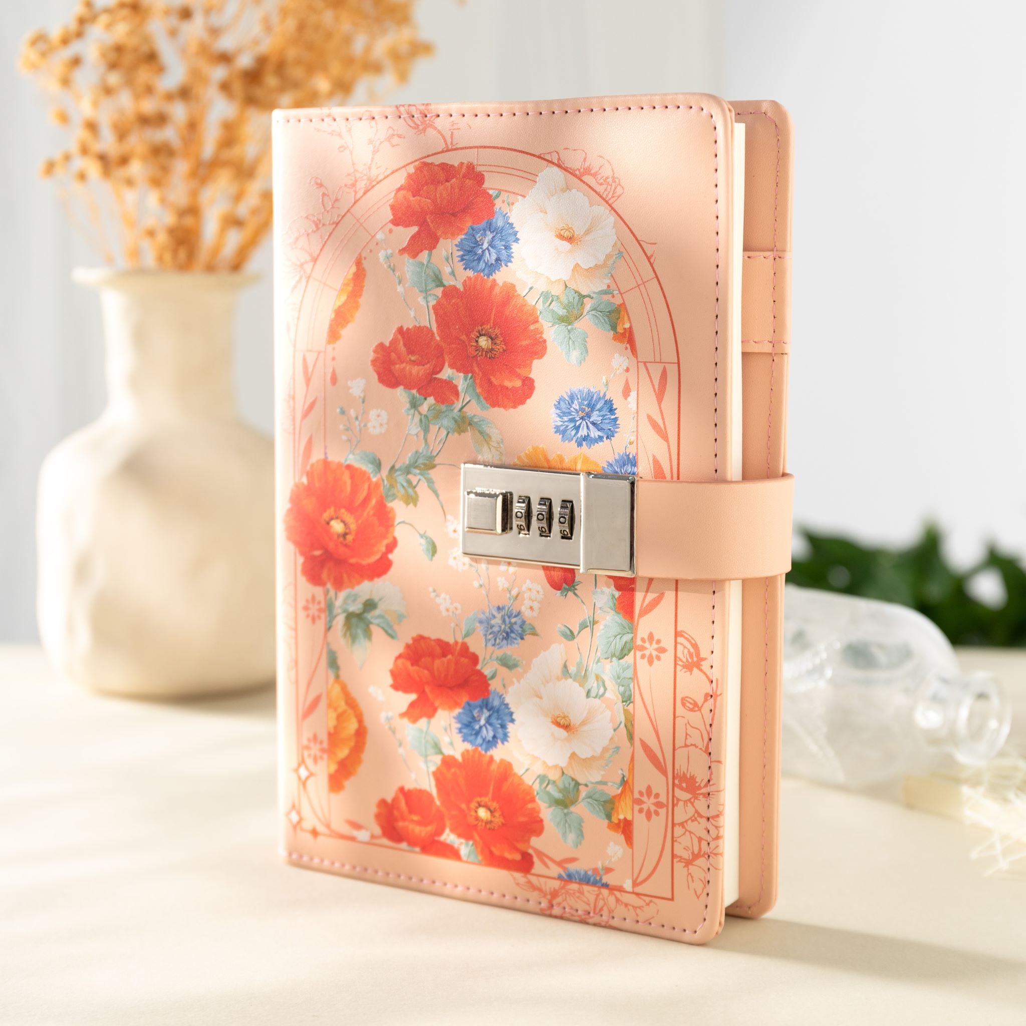 A5 orange vegan leather notebook with a 3-digit metal combination lock, featuring a colorful floral arch design, standing upright on a light desk with a dried flower vase in the background.