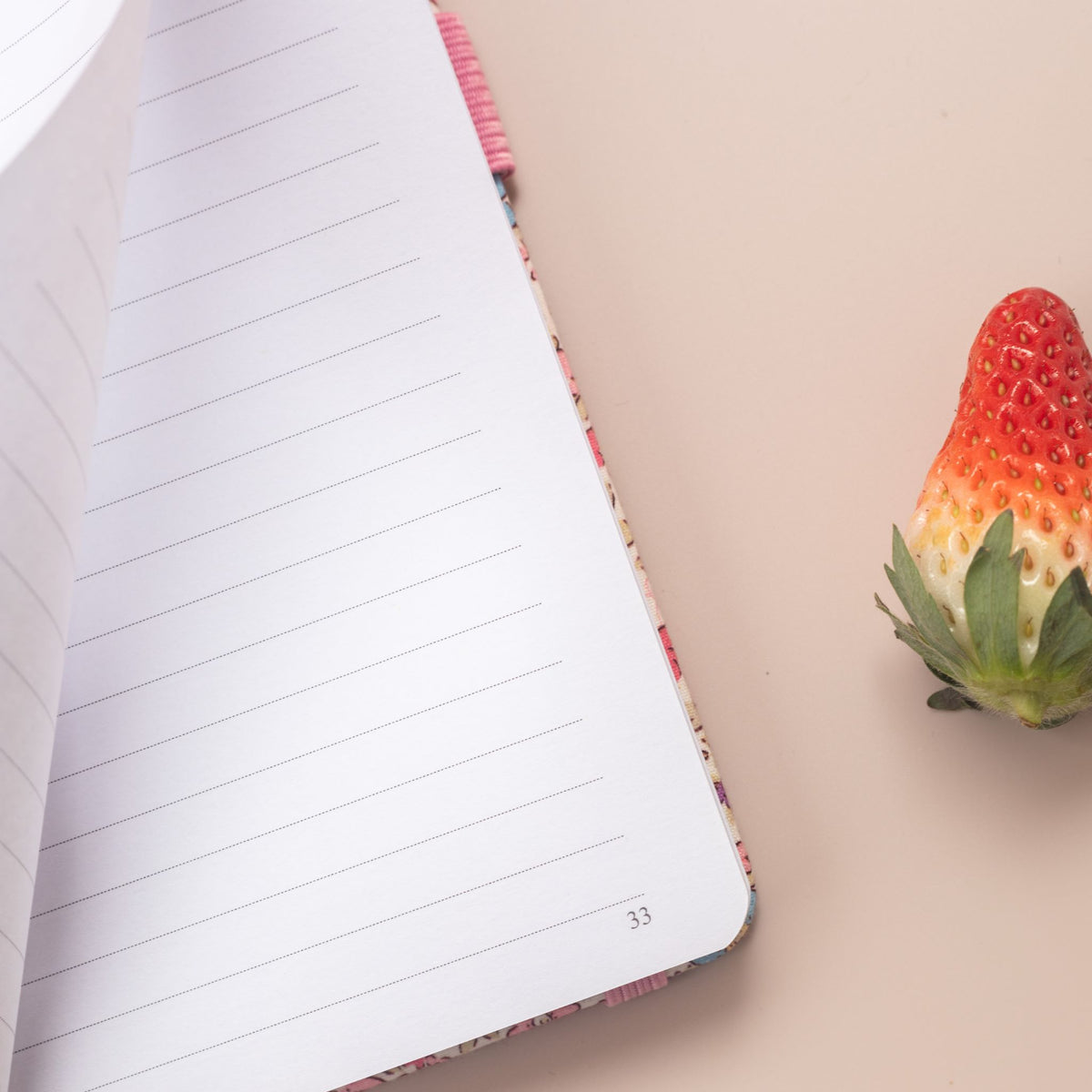 Close-up of a page being turned in the pink ditsy floral notebook, revealing the smooth lined paper interior and corner page number.