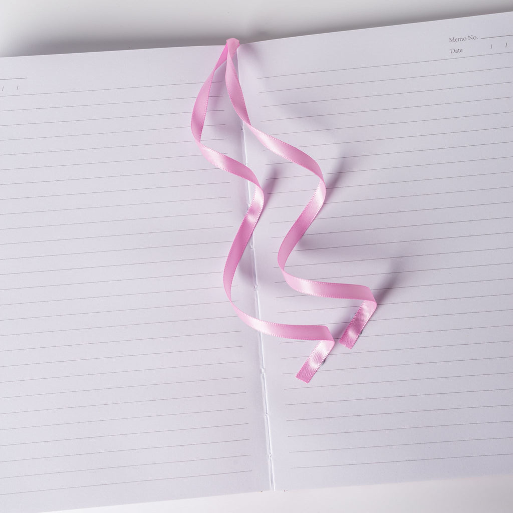Pink satin ribbon bookmark elegantly resting on the open lined pages of the pink ditsy floral notebook.
