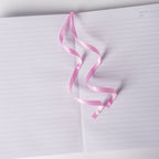 Pink satin ribbon bookmark elegantly resting on the open lined pages of the pink ditsy floral notebook.
