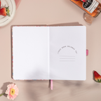 Open pink ditsy floral notebook showing the "THIS BOOK BELONGS TO" ownership page, laid flat on a pink surface with a pink ribbon bookmark.