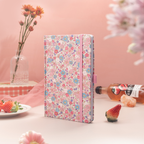 Pink ditsy floral fabric notebook standing upright on a pink desk, styled with fresh strawberries and a bottle of floral drink.