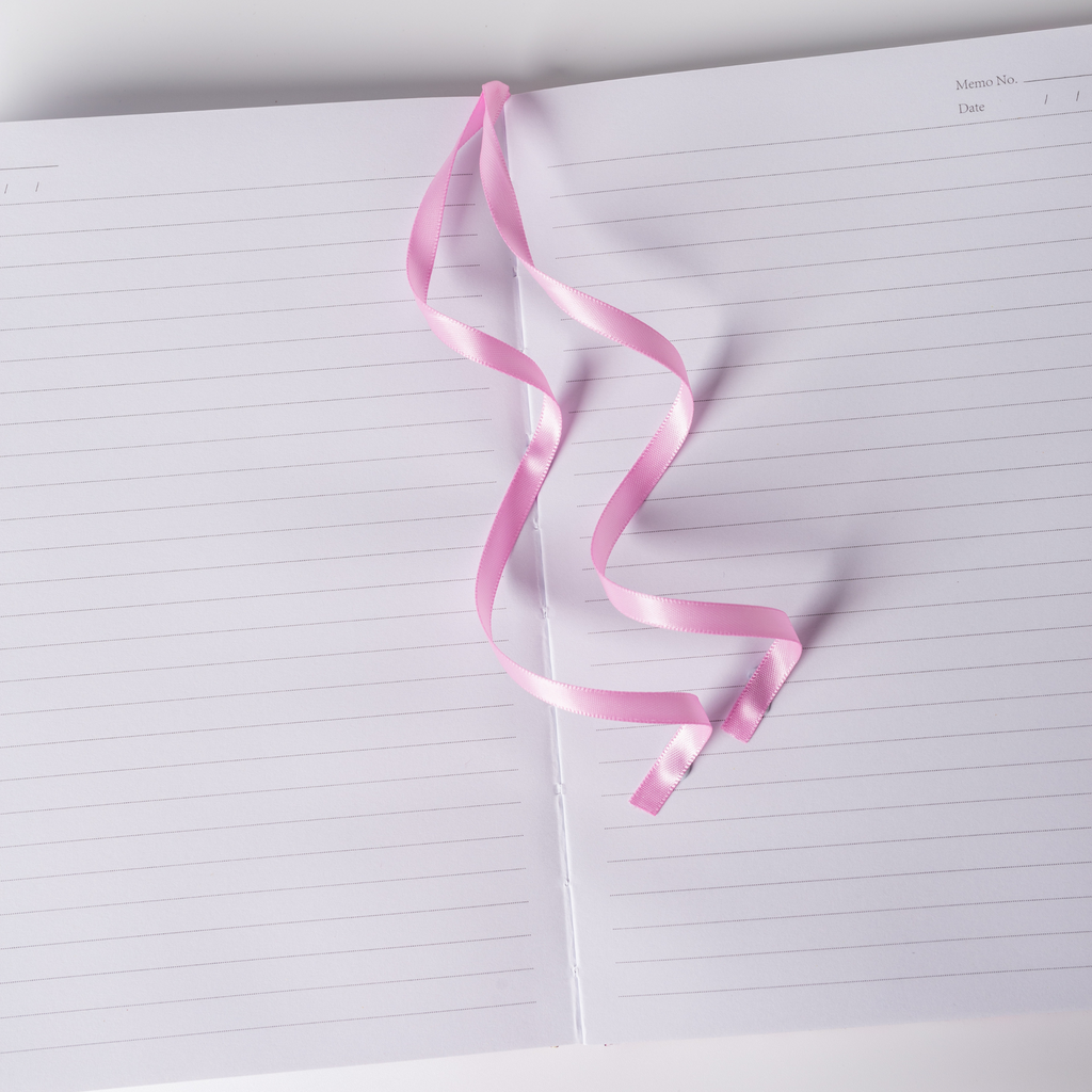 Pink satin ribbon bookmark elegantly resting on the open lined pages of the pink ditsy floral notebook.