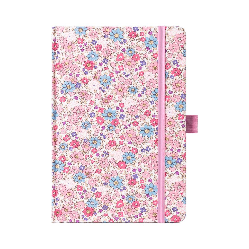 A5 pink ditsy floral fabric notebook standing upright on a white background, featuring a dense pattern of small pink and blue blossoms, finished with a matching pink elastic closure.
