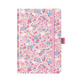 A5 pink ditsy floral fabric notebook standing upright on a white background, featuring a dense pattern of small pink and blue blossoms, finished with a matching pink elastic closure.