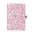 A5 pink ditsy floral fabric notebook standing upright on a white background, featuring a dense pattern of small pink and blue blossoms, finished with a matching pink elastic closure.