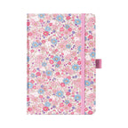 A5 pink ditsy floral fabric notebook standing upright on a white background, featuring a dense pattern of small pink and blue blossoms, finished with a matching pink elastic closure.
