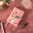 Top-down view of the pink floral vegan leather journal laid flat, showing the metal combination lock, pink ribbon, and pen.