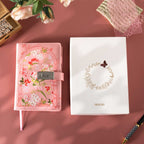 Pink floral vegan leather journal with lock placed next to its white gift box with a gold foil floral wreath logo.   