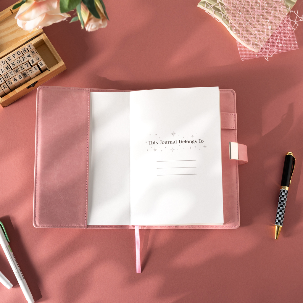  Open pink vegan leather notebook showing the "This Journal Belongs To" ownership page, laid flat with a matching pink ribbon.