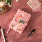 Top-down view of the pink floral vegan leather notebook laid flat, showing the metal combination lock, pink ribbon, and pen.