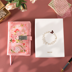 Pink floral vegan leather notebook with lock placed next to its white gift box with a gold foil floral wreath logo.   