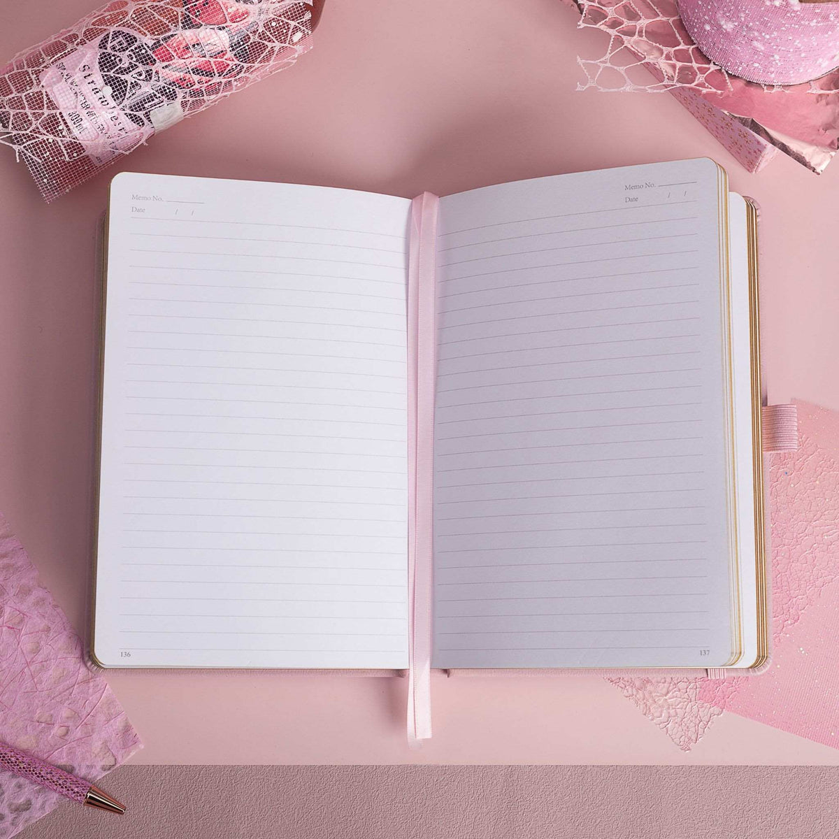 A5 line notebook opened flat on a pink desk, displaying clean white pages with a pink ribbon bookmark.