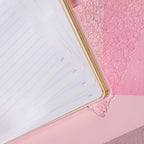 Open A5 notebook showing the 100gsm lined paper interior with golden borders, corner numbers, and a pink ribbon bookmark.