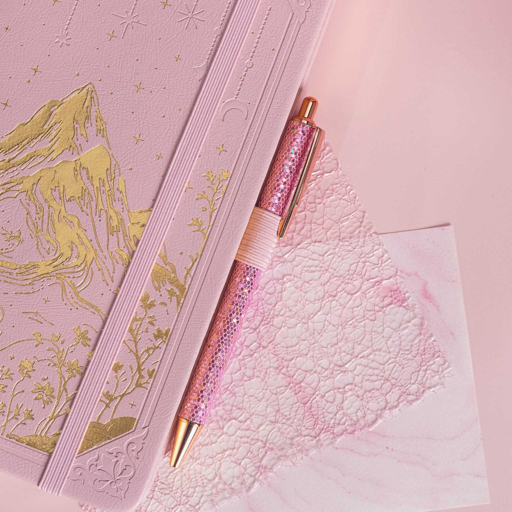Detail of the gold foil mountain embossing on the pink vegan leather cover, paired with a matching pink glitter pen.