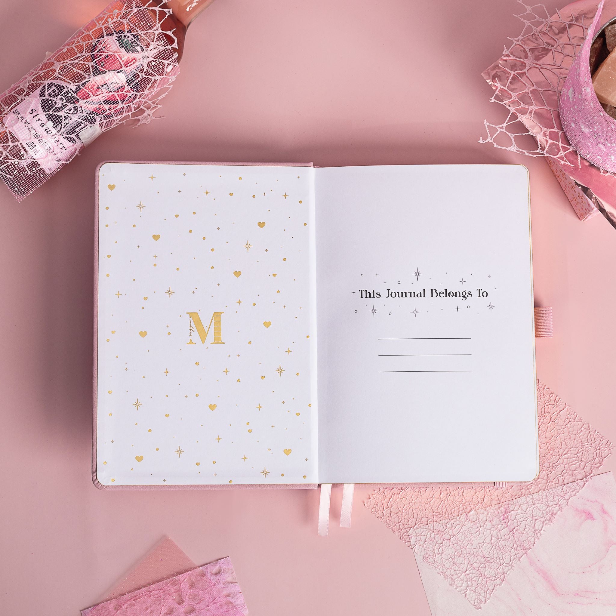 Inside front page of the pink notebook featuring a gold foil "M" logo on the left and "This Journal Belongs To" ownership section on the right.
