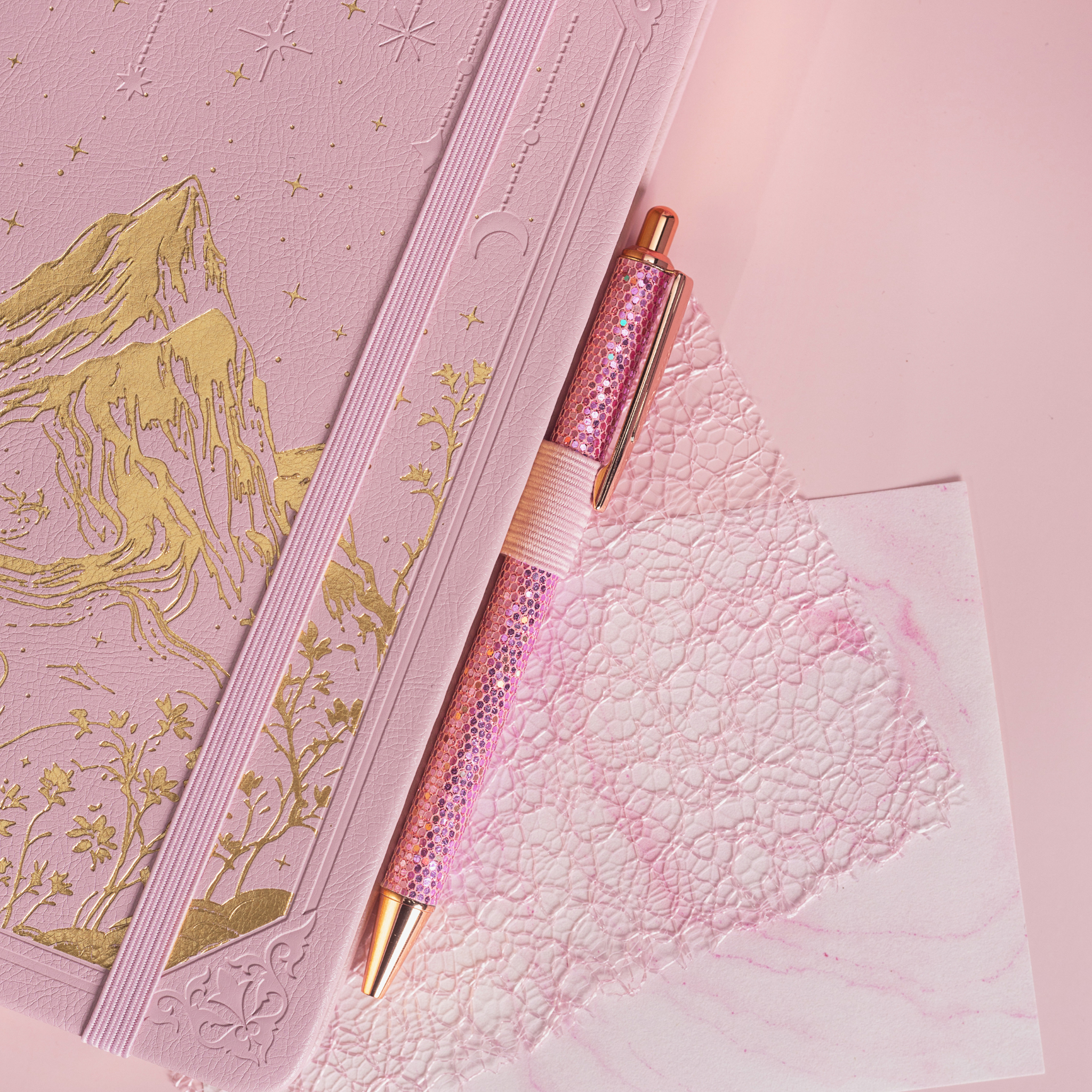 Detail of the gold foil mountain embossing on the pink vegan leather cover, paired with a matching pink glitter pen.
