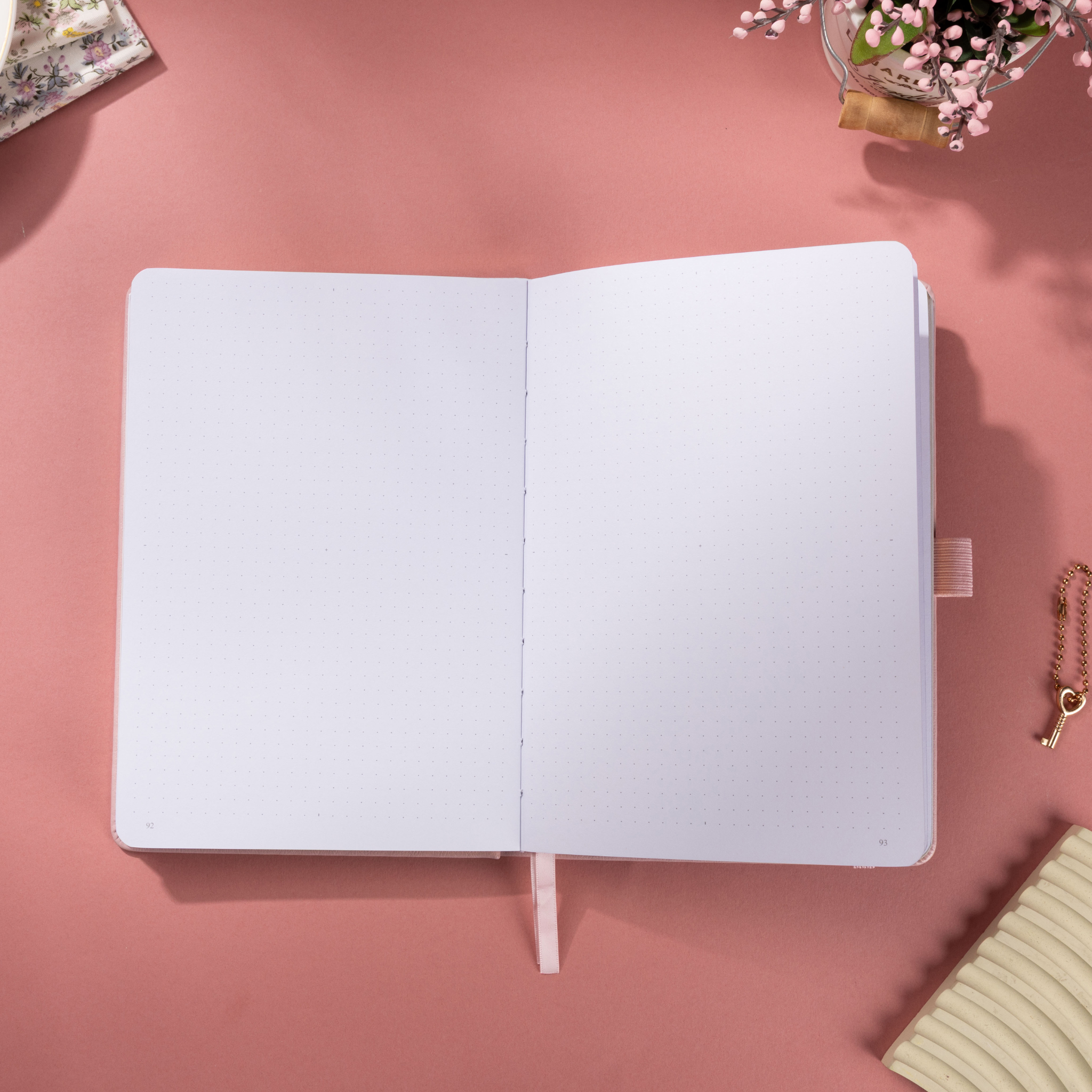 Open A5 journal showing the 160gsm dot grid paper interior, flat laid on a pink surface with a pink ribbon bookmark.