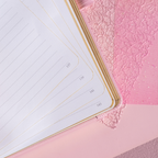 Open A5 notebook showing the 100gsm lined paper interior with golden borders, corner numbers, and a pink ribbon bookmark.
