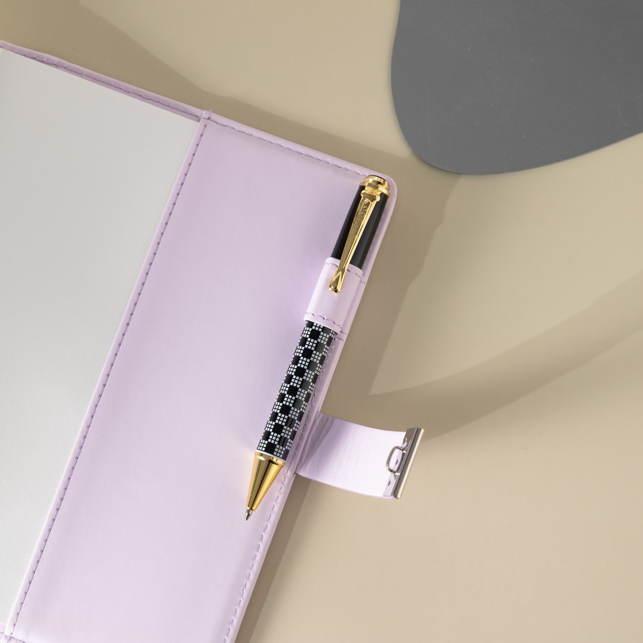 Close-up of the purple vegan leather journal, showing a black and white patterned pen tucked into the side pen loop, with the metal lock strap extended and visible stitching details on the cover.