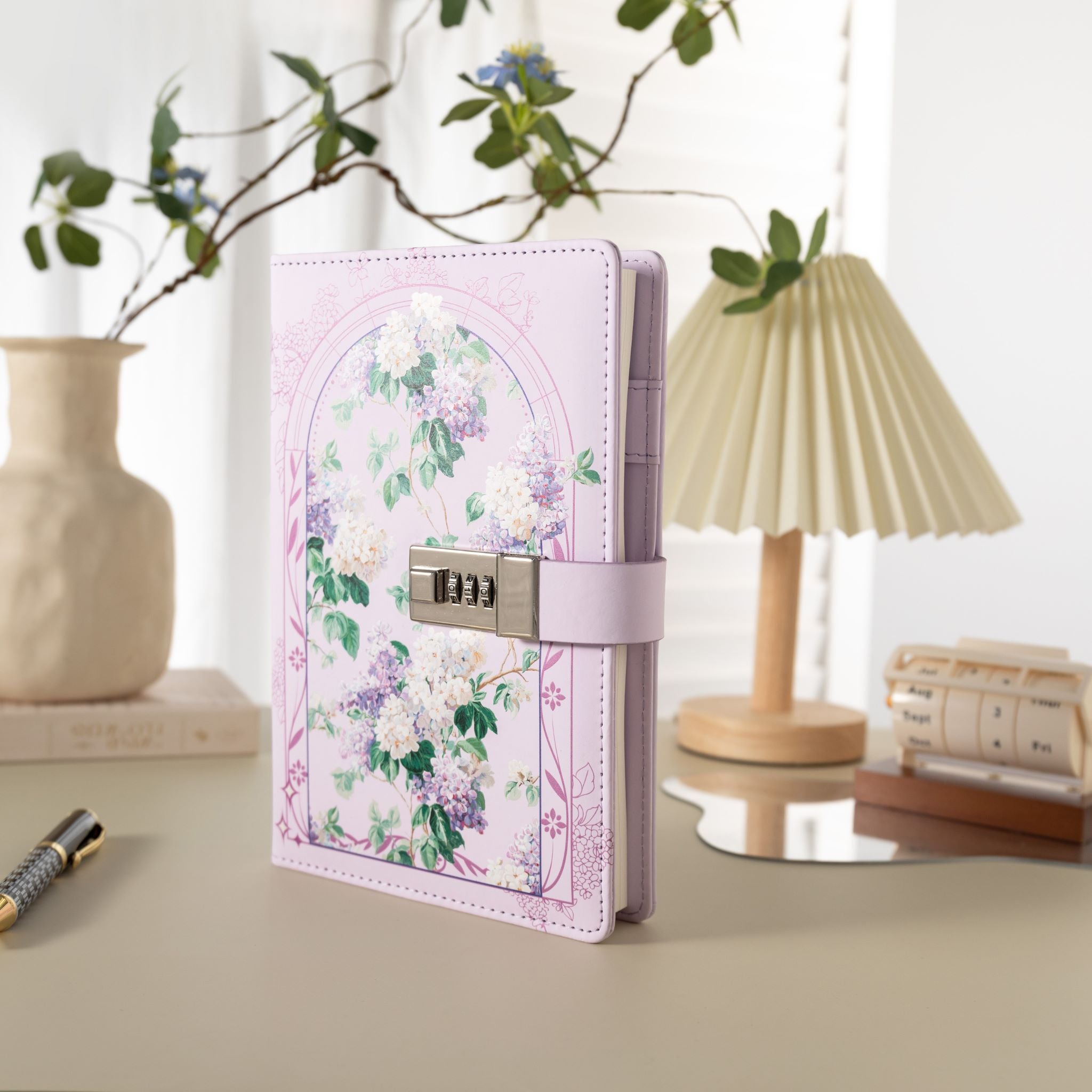 Purple floral vegan leather journal with a metal password lock, standing upright on a light beige desk with a lamp and plant.