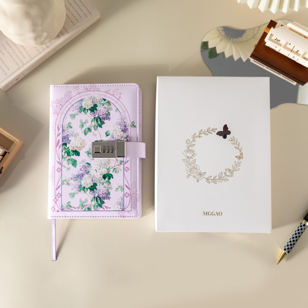 Purple floral vegan leather notebook with lock placed next to its white gift box with a gold foil wreath logo.