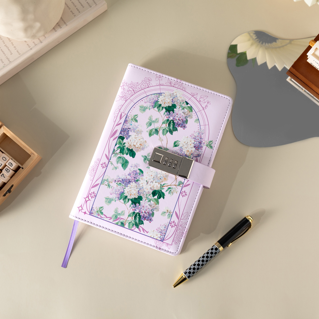 Top-down view of the purple floral vegan leather notebook laid flat on a beige surface, featuring a botanical arch design, a 3-digit metal combination lock, a purple ribbon bookmark, and styled with a patterned pen and wooden stamps.