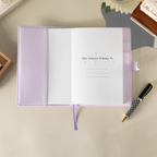 Open purple vegan leather notebook showing the "This Journal Belongs To" ownership page, laid flat with a matching purple ribbon and a pen.