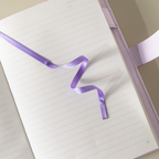 Close-up of the open lined paper interior with a purple satin ribbon bookmark and a pen.