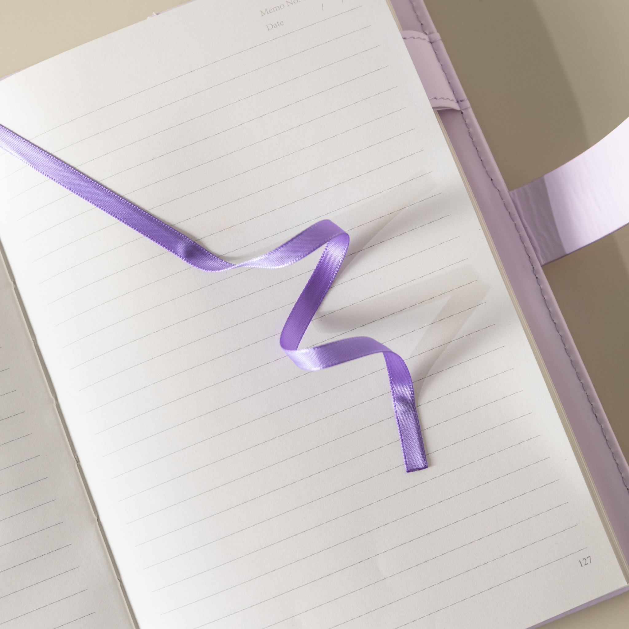 Close-up of the open lined paper interior with a purple satin ribbon bookmark and a pen.