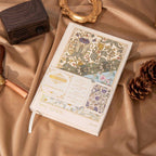 A5 Wind Flowers Hardcover Lined Notebook Flat Lay on Wooden Desk with Pinecones and Gold Decor