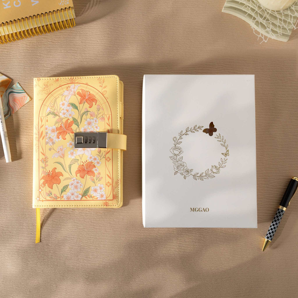 Yellow floral vegan leather journal with lock placed next to its white gift box with a gold foil wreath logo.