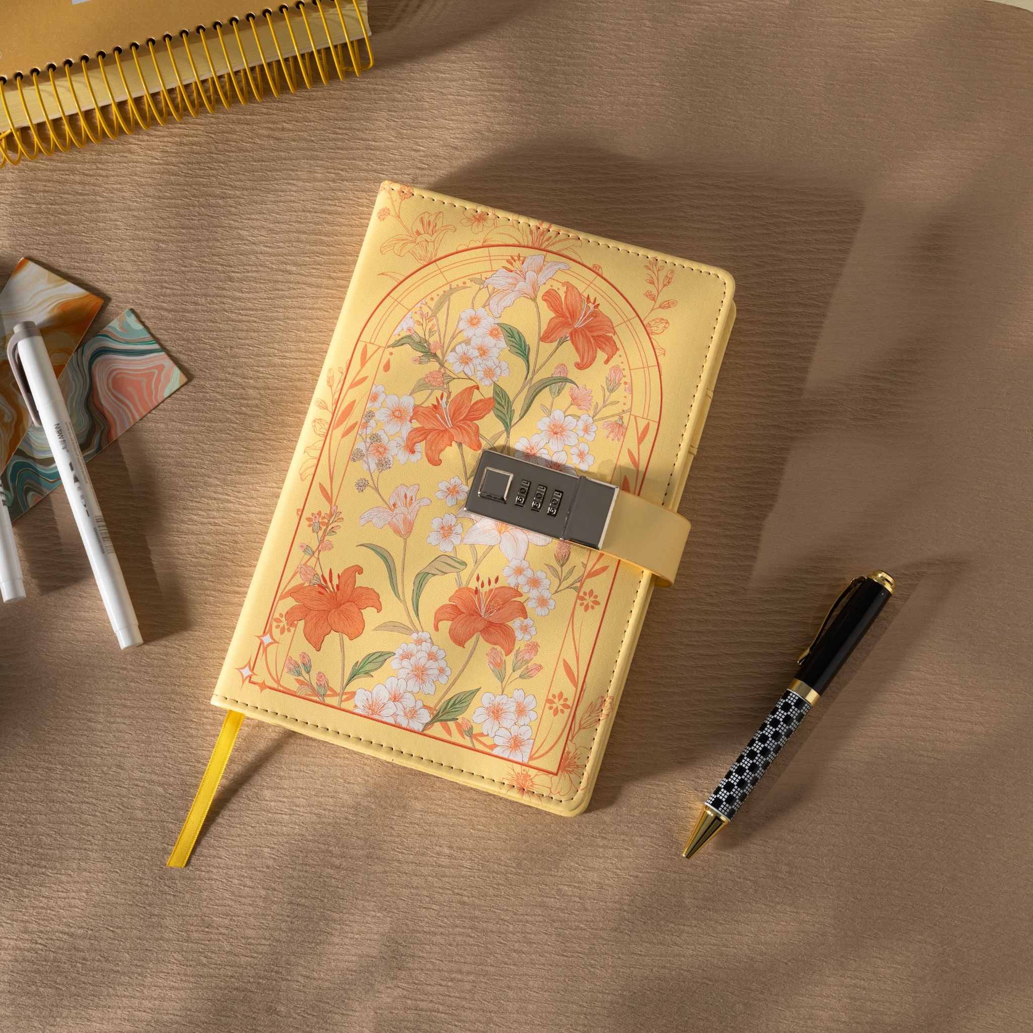 Top-down view of the yellow floral vegan leather notebook laid flat, showing the metal lock and a yellow ribbon.