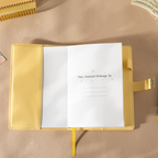 Open yellow vegan leather notebook showing the "This Journal Belongs To" ownership page, laid flat with a matching yellow ribbon.