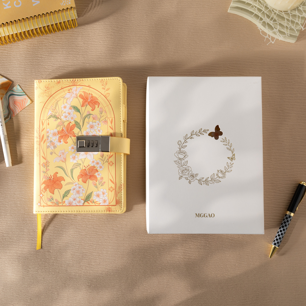 Yellow floral vegan leather notebook with lock placed next to its white gift box with a gold foil wreath logo.