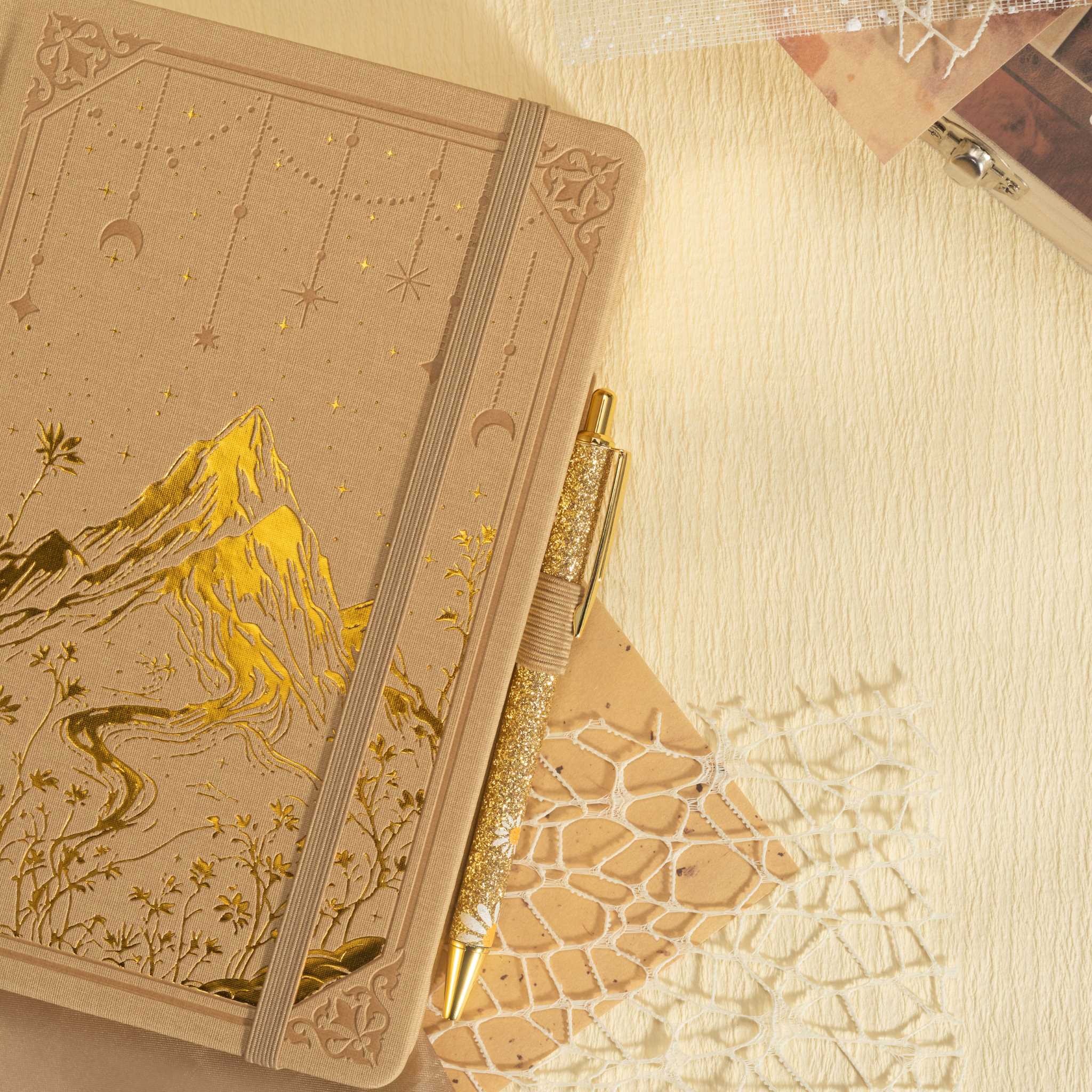 Beige vegan leather journal laid flat with a matching pen and dried flowers, showcasing the gold foil mountain cover design.