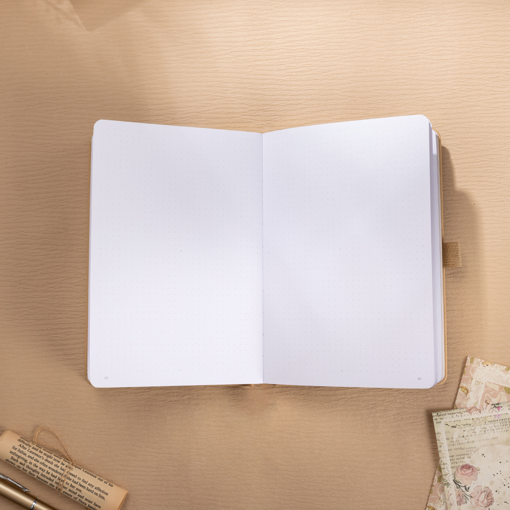 Open A5 journal laid flat on a wooden surface, displaying the clean 160gsm dot grid paper interior with a beige ribbon bookmark.