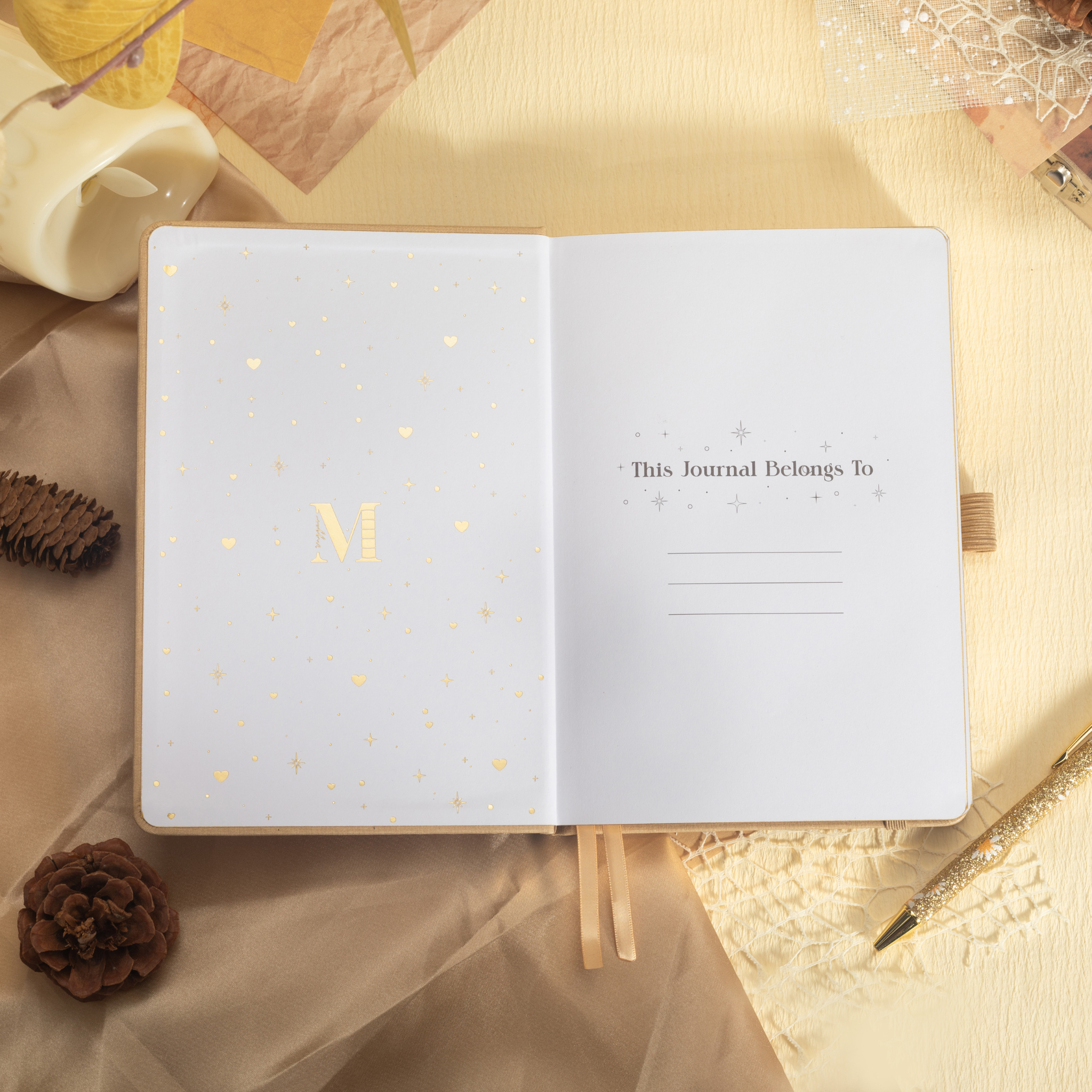 Inside front page of the beige mountain journal featuring a gold foil "M" logo and "This Journal Belongs To" ownership section.