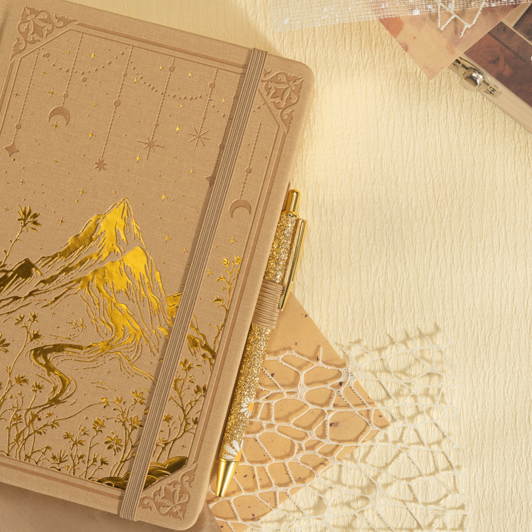Beige vegan leather journal laid flat with a matching pen and dried flowers, showcasing the gold foil mountain cover design.