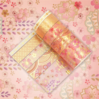 Pink and gold blossom washi tapes partially unrolled on a pastel cherry blossom background, displaying elegant gold foil geometric lattice, flowing wave patterns, and delicate floral motifs.